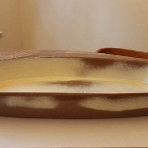 Puede incluir: Un plato rectangular de cerámica con un esmalte marrón claro y un esmalte blanco en el interior. El plato tiene un fondo ligeramente redondeado y un borde ancho y plano.