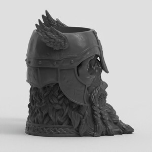 May include: A dark gray, cylindrical vessel shaped like a bearded warrior wearing a winged helmet. The design features intricate sculpted details including a braided beard, a textured helmet with side wings, and a smooth, open top rim for storage.