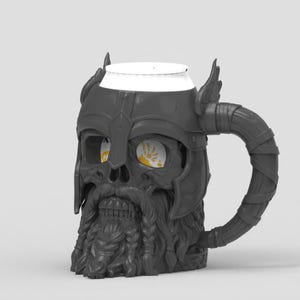 May include: A dark gray mug shaped like a skull wearing a winged helmet and a braided beard. The mug features a curved handle and a white rim at the top. Through the hollow eye sockets, a yellow graphic with a white wing design is visible.