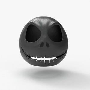 May include: A black, spherical sculpture of a character's head with large, hollow eye sockets and a stitched-on grin. The head is smooth and matte, with a slight shadow beneath it, suggesting it is floating.