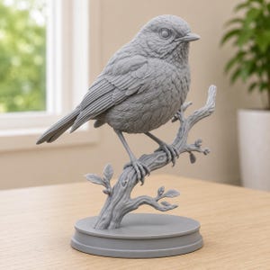 May include: A monochromatic grey figurine of a small bird perched on a textured tree branch. The bird features detailed feather textures and a sharp beak. The entire sculpture is mounted on a smooth, circular base, showcasing a uniform matte finish.