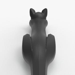 May include: A black cat-shaped bottle stopper, viewed from the back. The stopper has a sleek, matte finish and features pointed ears and a stylized body. The design is minimalist and modern, suitable for wine bottles.