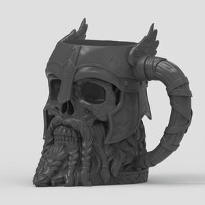 May include: A dark gray mug shaped like a skull wearing a winged helmet. The skull features a detailed beard with braided sections and a mustache. The handle is curved and wrapped with a textured band, resembling a horn or a leather-bound grip.