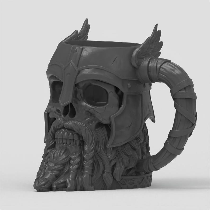May include: A dark gray mug shaped like a skull wearing a winged helmet. The skull features a detailed beard with braided sections and a mustache. The handle is curved and wrapped with a textured band, resembling a horn or a leather-bound grip.