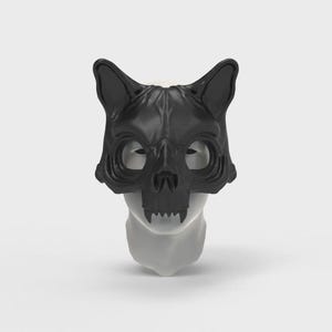 May include: A black cat skull mask with pointed ears, eye sockets, and a detailed skull design. The mask is made of a smooth, dark material and is displayed on a white mannequin head. The mask has a menacing appearance.