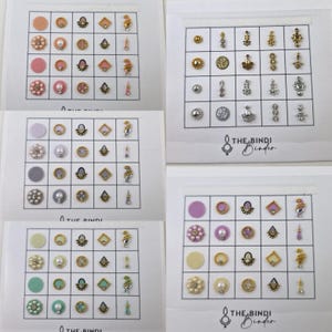 May include: Four sheets of adhesive bindis with various designs and colours. Each sheet has 16 bindis in a grid pattern. The bindis are in shades of pink, purple, white, and green. The bindis are decorated with pearls, rhinestones, and gold accents. The text "THE BINDI Binder" is printed on each sheet.