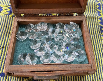 May include: A wooden box with a hinged lid is open, revealing a green felt lining and a collection of clear glass crystal prisms.