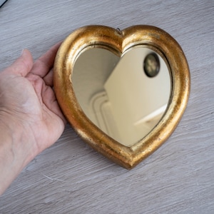 May include: A heart-shaped wall mirror featuring a thick, textured gold-toned frame with a distressed finish. The reflective glass surface is set within the center of the heart, and a small metal hanging loop is visible at the top of the frame.