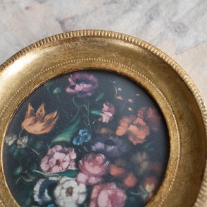 Focused view of the top edge and inner detail of the gilded wooden photo frame with floral insert.