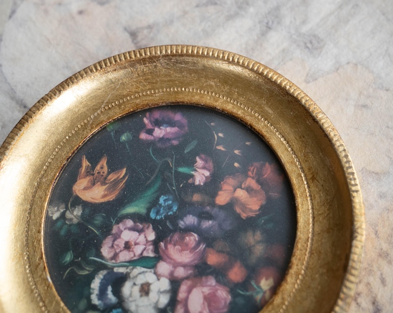 Focused view of the top edge and inner detail of the gilded wooden photo frame with floral insert.