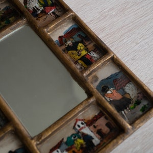 May include: A gold-framed mirror with multiple small windows featuring hand-painted scenes of people and buildings. The mirror is surrounded by a decorative frame with a gold finish.
