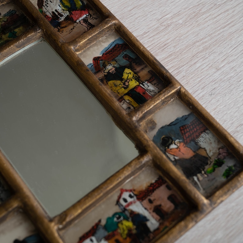 May include: A gold-framed mirror with multiple small windows featuring hand-painted scenes of people and buildings. The mirror is surrounded by a decorative frame with a gold finish.