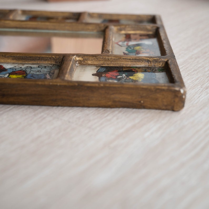 May include: A gold-toned wooden picture frame with a mirror in the centre and small colourful images in the surrounding panels.