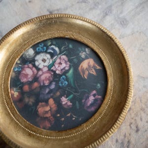 Direct close-up view of the artwork within the round gold frame, showing vibrant flowers against a dark background.