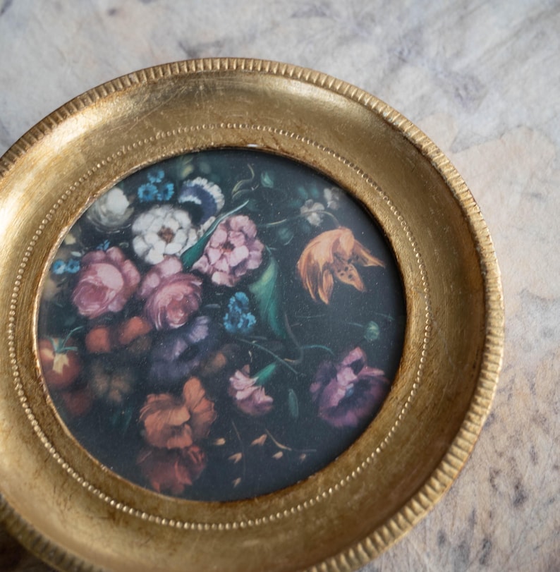 Direct close-up view of the artwork within the round gold frame, showing vibrant flowers against a dark background.