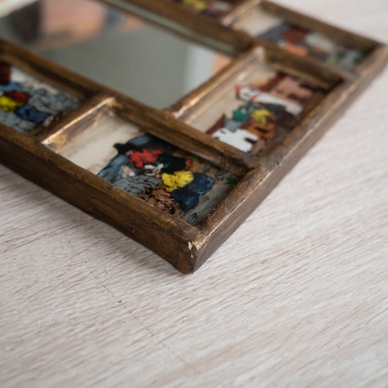 May include: A gold-toned wooden frame with a mirror in the centre and multiple smaller framed images of people in colourful clothing. The frame has a distressed look.