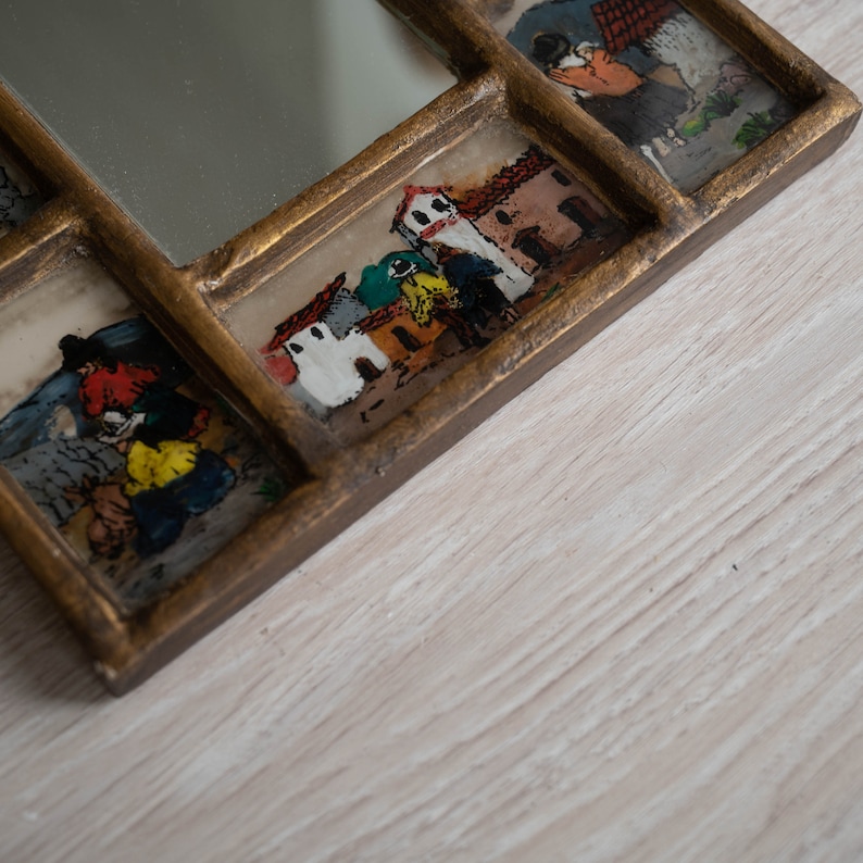 May include: A wooden framed mirror with multiple small panes, each containing a painted scene of a village with houses and people. The mirror is gold-toned and has a distressed finish.