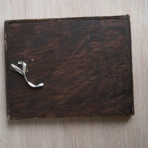 May include: A dark brown wooden frame with a white piece of tape attached to the top left corner.