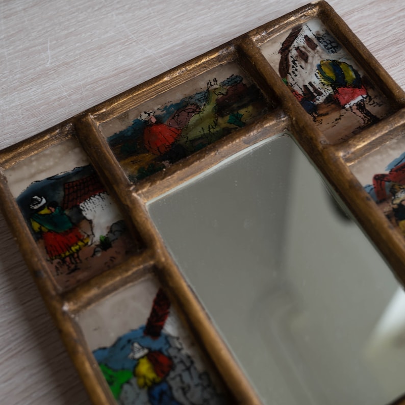May include: A gold framed mirror with a central mirror surrounded by eight smaller glass panels, each with a different hand-painted scene. The scenes are colourful and depict people and animals.