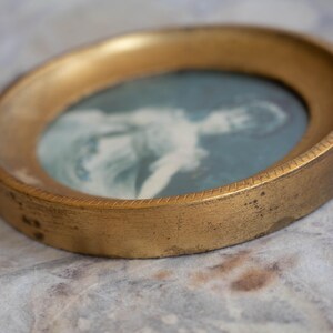May include: A gold-toned oval picture frame with a faded image of a person inside. The frame has a decorative edge.