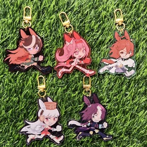 Könnte beinhalten: Fünf Schlüsselanhänger aus Acryl mit Anime-Charakteren in dynamischen Laufposen. Jeder Schlüsselanhänger hat einen goldfarbenen Verschluss. Die Charaktere haben unterschiedliche Haarfarben und Outfits, vor dem Hintergrund von grünem Gras.