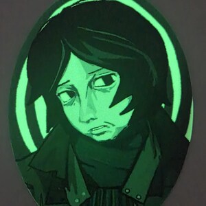 Puede incluir: Obra de arte ovalada que representa a una persona con cabello oscuro y una expresi&oacute;n sombr&iacute;a. La obra es principalmente verde, con un efecto brillante alrededor de la figura y un fondo oscuro. La persona lleva un abrigo oscuro.