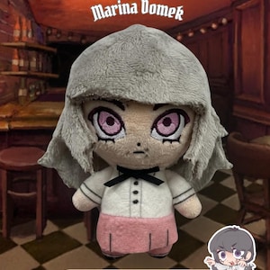 Puede incluir: Un peluche de Marina Domek de Fear and Hunger: Termina, con cabello gris, ojos rosas, camisa blanca con lazo negro y falda rosa. El peluche mide 10,16 cm, tiene una cadena de bolas e incluye una pegatina gratuita.