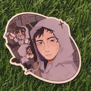 Könnte beinhalten: Aufkleber mit einer Cartoon-Illustration einer Person in einem grauen Kapuzenpullover mit einem roten Kreuz auf der Kapuze. Zwei kleinere Figuren mit blutigen Gesichtern befinden sich im Hintergrund. Der Aufkleber befindet sich auf einer grünen Oberfläche.