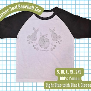 May include: Light blue baseball tee with black sleeves. The shirt features a graphic of three seals with the text "Harbor Seal" above the design. The shirt is 100% cotton and available in sizes S, M, L, XL, and 2XL.