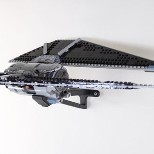 Może przedstawiać: Model Lego Star Wars TIE Interceptor w kolorze czarnym i szarym z szarym stojakiem. Model jest pochylony w prawo, a skrzydła są rozłożone.