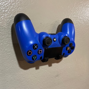 May include: A blue PlayStation 4 controller mounted on a wall. The controller has a black faceplate with the PlayStation logo and buttons.