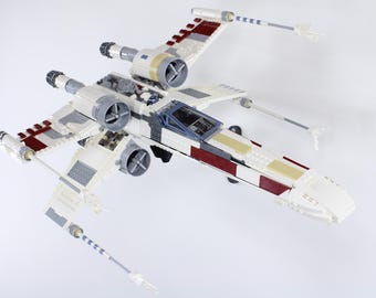 May include: A white and red Lego X-Wing Starfighter with a cockpit and two laser cannons. The model is built with Lego bricks and has a detailed design.