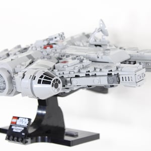 May include: A white Lego Millennium Falcon starship model with red accents, displayed on a black stand. The model features detailed design and intricate details, including the iconic cockpit and engine exhaust.