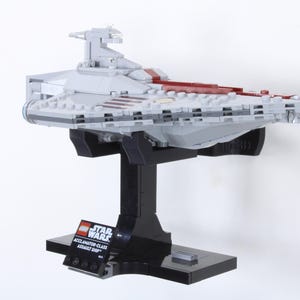 May include: A gray and red Lego Star Wars Accalamator-Class Assault Ship model displayed on a black stand. The model has intricate details and is mounted on a black base with a Star Wars logo.