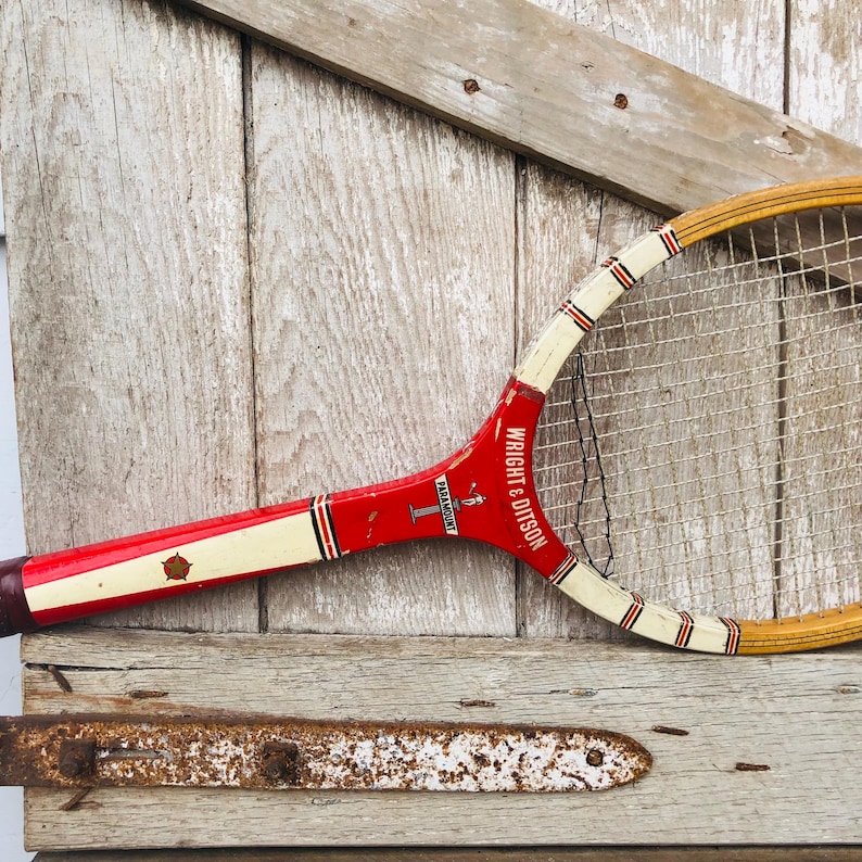 May include: A vintage red and white tennis racket with a wooden frame. The racket has a white stripe with the text "PARAMOUNT" and "WRIGHT & DITSON" printed on it.