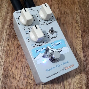 May include: A light gray guitar effects pedal with white knobs and the text "mont blanc". The pedal has a mountain graphic and the words "Flexible EQ + Boost". It is labeled "Handbuilt in the UK by midboost".