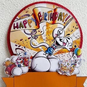 Könnte beinhalten: Ein farbenfroher Tortenaufsatz zum Geburtstag mit einer Cartoon-Maus, die einen Zauberstab und ein Banner mit der Aufschrift "Happy Birthday!" hält. Der Aufsatz hat einen roten Glitzerrahmen und ein orangefarbenes Banner.