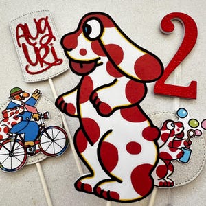 Puede incluir: Decoraciones de cumpleaños con un perro de dibujos animados con lunares rojos sobre fondo blanco. Incluye un número 2 rojo con purpurina, un letrero con la palabra "Auguri" y un perro soplando burbujas.