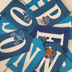 K&ouml;nnte beinhalten: Blau-wei&szlig;e Girlande mit dem Wort "ONE" in wei&szlig;en Buchstaben. Jeder Buchstabe hat einen blauen Stitch-Charakter aus dem Disney-Film Lilo & Stitch. Stitch h&auml;lt einen Geburtstagskuchen, einen Teller mit Essen und einen Hamburger.