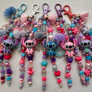 May include: A collection of colorful keychains featuring Stitch characters. Each keychain has a different color scheme, with beads, charms, and a fluffy tassel. The keychains are adorned with hearts, stars, and other decorative elements.