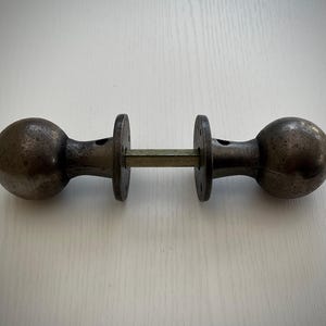May include: A pair of antique door knobs with a round, ball-shaped design. The knobs are made of metal and have a dark, aged finish.