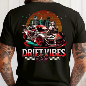Op de afbeelding: Zwart T-shirt met een afbeelding van een rood-grijze sportwagen, een anime-vrouw, een zonsondergang en een skyline. De tekst "DRIFT VIBES Only" staat onder de auto.