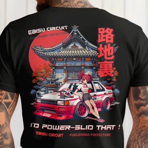 May include: Black t-shirt featuring a graphic of a red and white car with a Japanese anime-style illustration. The shirt includes text that reads "EBISU CIRCUIT FUKUSHIMA PREFECTURE" and "I'D POWER-SLID THAT!"