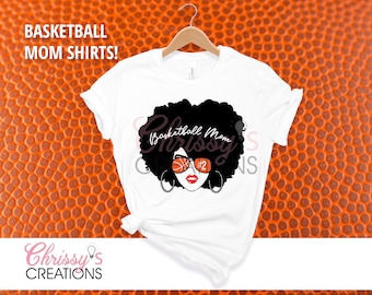 Pode incluir: Camiseta branca com um gráfico em preto e branco de uma mulher com afro usando óculos de sol com tema de basquete. O texto "Basketball Mom" está escrito em uma fonte estilizada.