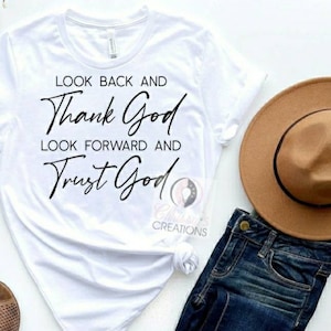Pode incluir: Camiseta branca com o texto "Look back and thank God, look forward and trust God" em letras pretas.