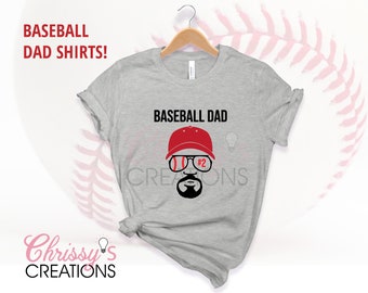 Pode incluir: Camiseta cinza com um gráfico de pai de beisebol. O gráfico apresenta um homem usando um boné de beisebol vermelho, óculos de sol e barba. O texto "Baseball Dad" está acima do gráfico.