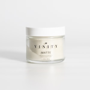 Pode incluir: Um frasco de vidro transparente com tampa branca, contendo uma subst&acirc;ncia bege clara. O frasco tem um r&oacute;tulo preto com as palavras "VINITY" e "MATTE". O r&oacute;tulo tamb&eacute;m inclui o texto "MEDIUM HOLD & NO SHINE" e "VEGAN & CRUELTY FREE". O frasco cont&eacute;m 56 g.