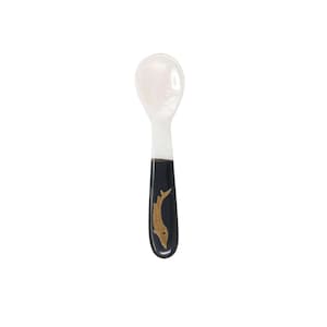 May include: A white mother of pearl spoon with a black handle and a gold fish design.