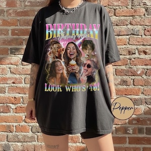 Op de afbeelding: Zwart T-shirt met een kleurrijke afbeelding met de tekst "BIRTHDAY Jessica's 40th" en "LOOK WHO'S 40!". De afbeelding toont afbeeldingen van lachende vrouwen. Het shirt heeft een casual, oversized stijl.