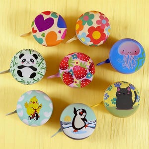 May include: Nine decorative bicycle bells with diverse patterns, such as hearts, flowers, and a panda. Other designs include strawberries, a cat, a penguin, and a chick. Each bell has a small lever.